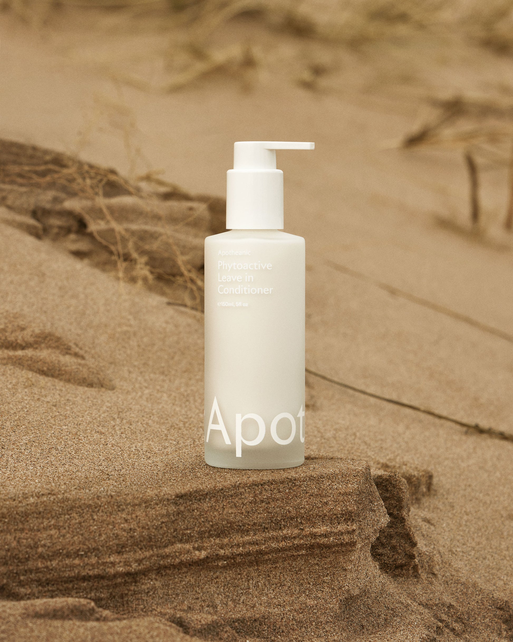 Apotheanic Phytoactive Leave in Conditioner, leave in treatment for dry and damaged hair. bottle in sand picture